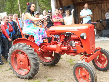  Tässä kuvassa hän nostelee helmansa punaiseen kulkupeliin, ja eikös vain valmiiksi käynnistetty traktori lähtee varmasti liikkeelle.